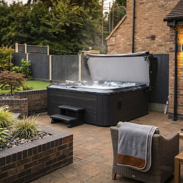 Hot tub in a backyard setting with a brick building and garden.