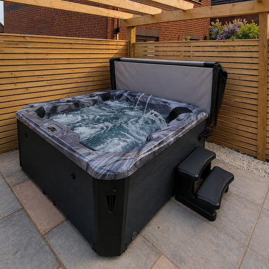 Hot tub with water features on a patio area with wooden fence and plants in the background