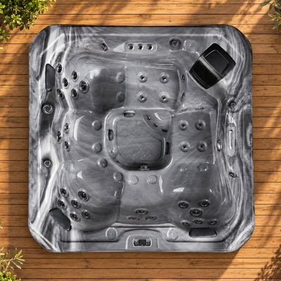 A top-down view of a gray and black marble-patterned hot tub on a wooden deck with plants in the corners.