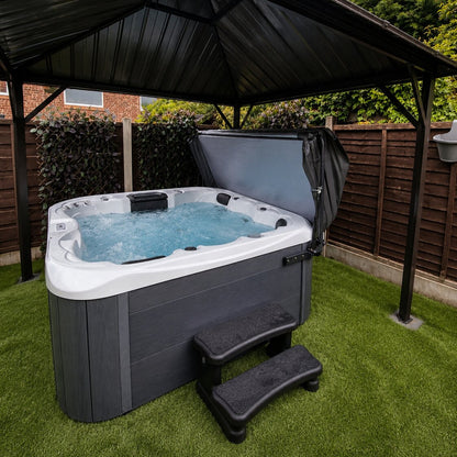 Hot tub with a black cover on grass under a wooden gazebo