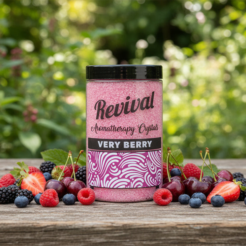 Jar of 'Revival Aromatherapy Crystals Very Berry' surrounded by berries on a wooden surface with a blurred green background